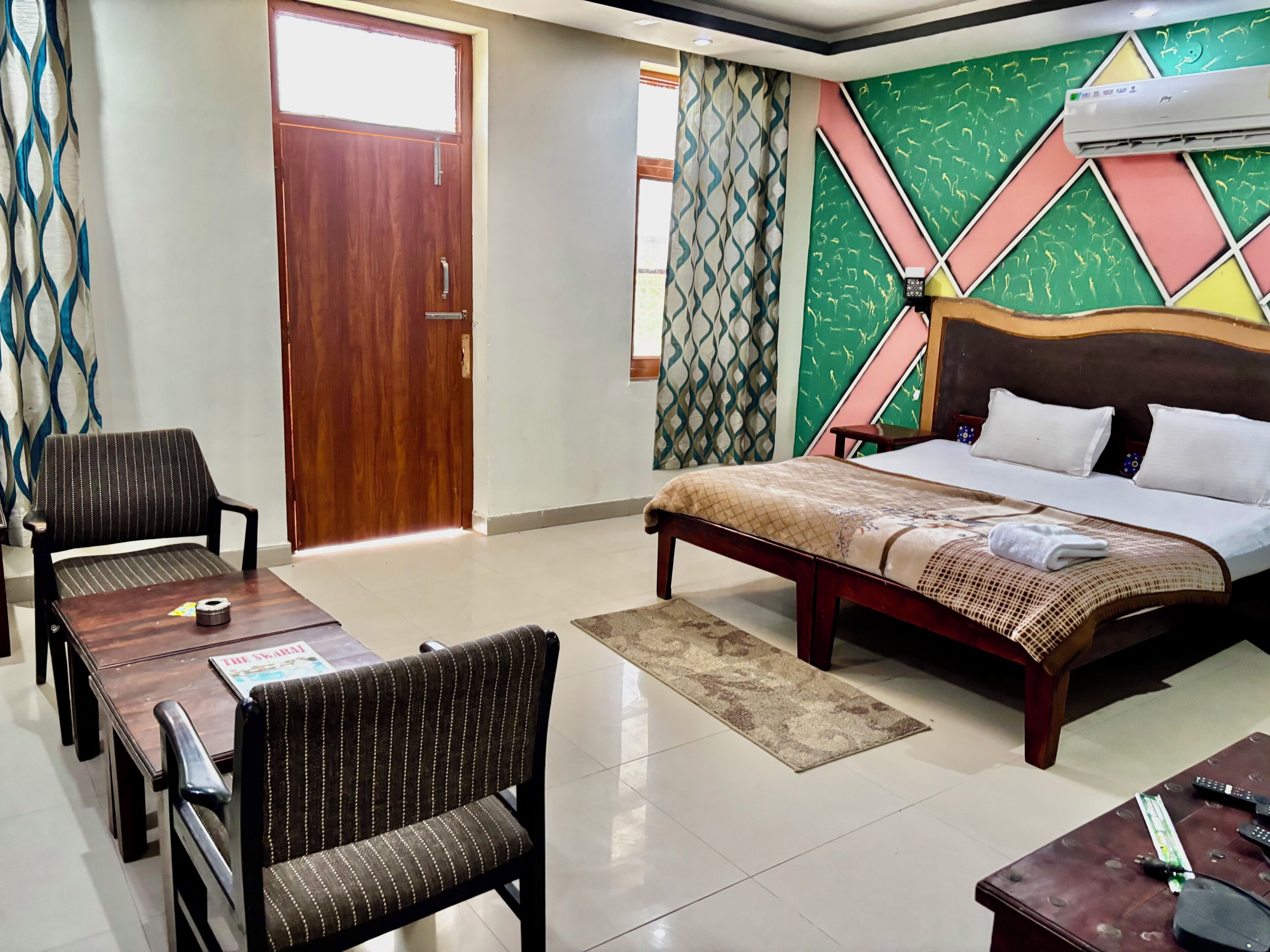 Une chambre d’hôtel avec un lit, un bureau avec des chaises, une porte en bois et des murs à motifs.