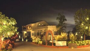 Un hotel de dos pisos, con un acceso cubierto y un jardín ajardinado con iluminación.