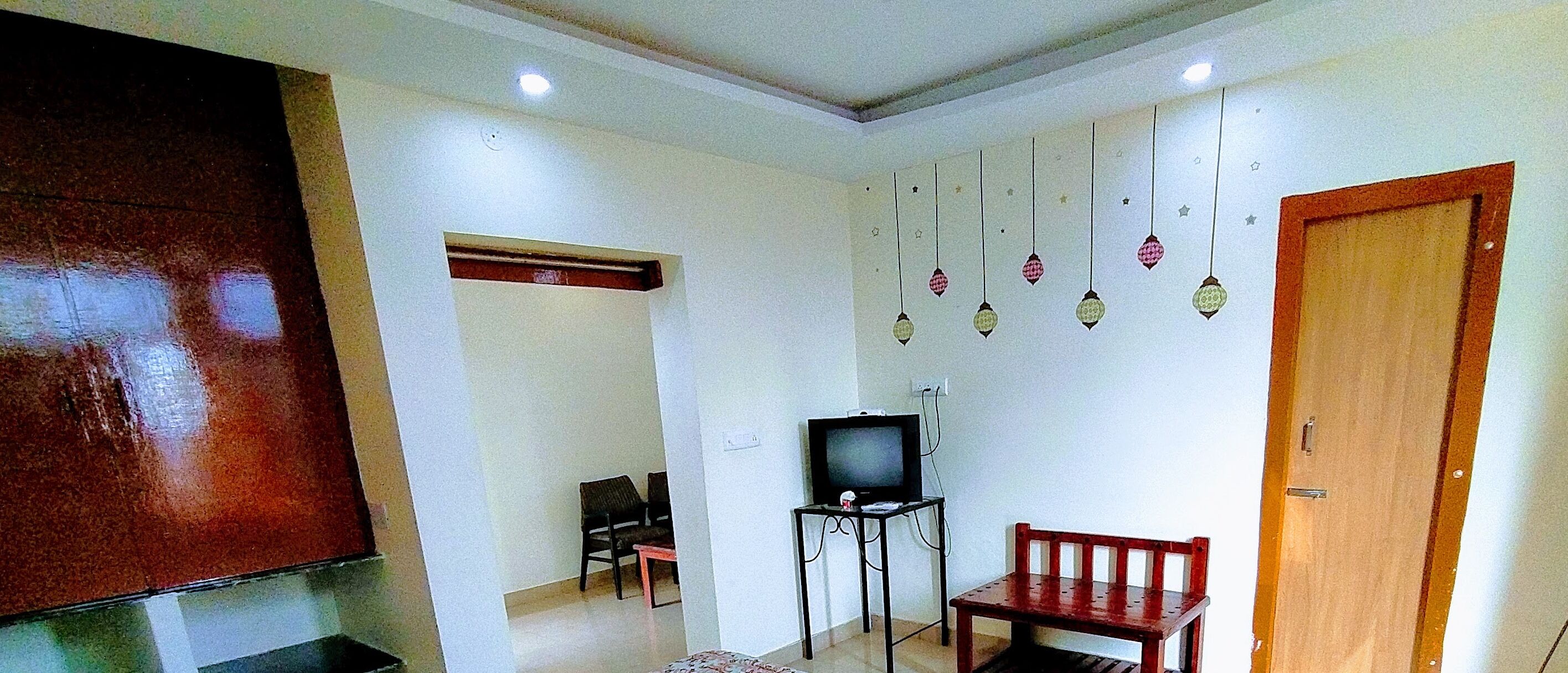 Una sala de estar con un televisor sobre un mueble bajo, una puerta de madera y una lámpara fijada a la pared.