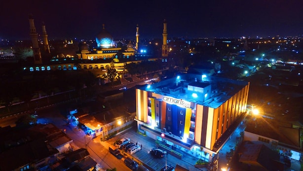 A modern hotel with a prominent sign, surrounded by a cityscape at night. - Amaris Hotel Pekanbaru (Pekanbaru)