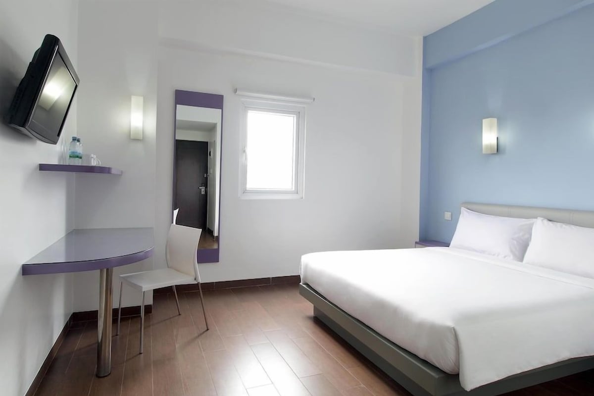Une chambre d’hôtel équipée d’un lit, d’un bureau, d’une chaise, d’une télévision, d’une fenêtre et d’un miroir.