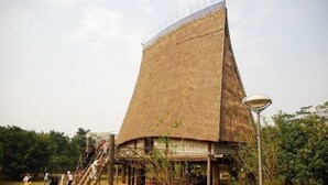 A traditional thatched-roof structure with a staircase leading up to it, surrounded by a grassy area with trees. - Rendez Vous Hotel (Hanoi)