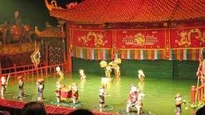 A traditional performance with performers in colorful costumes on a stage with a red roof and decorative elements. - Rendez Vous Hotel (Hanoi)