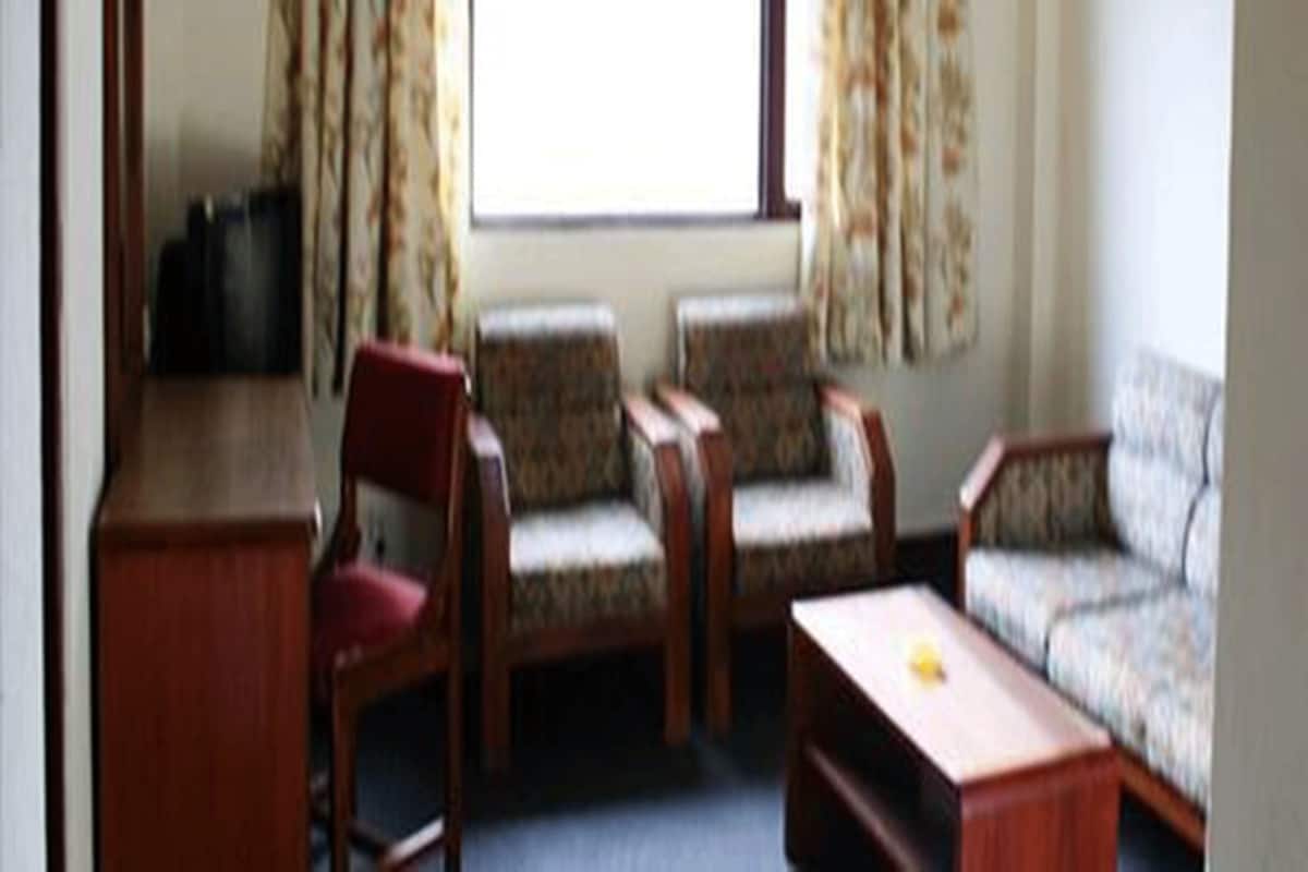 Ein Zimmer mit einem Holztisch, zwei gemusterten Sessel, einem roten Stuhl und einem Sofa.