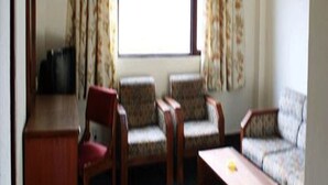 Ein Zimmer mit einem Holztisch, zwei gemusterten Sessel, einem roten Stuhl und einem Sofa.