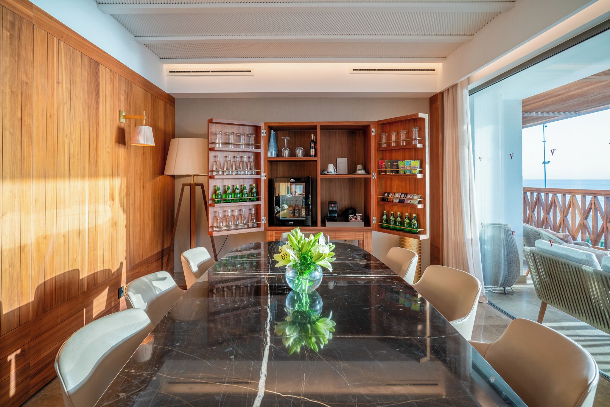 Een vergaderruimte met een marmeren tafel, stoelen, een koffieapparaat en een minibar.