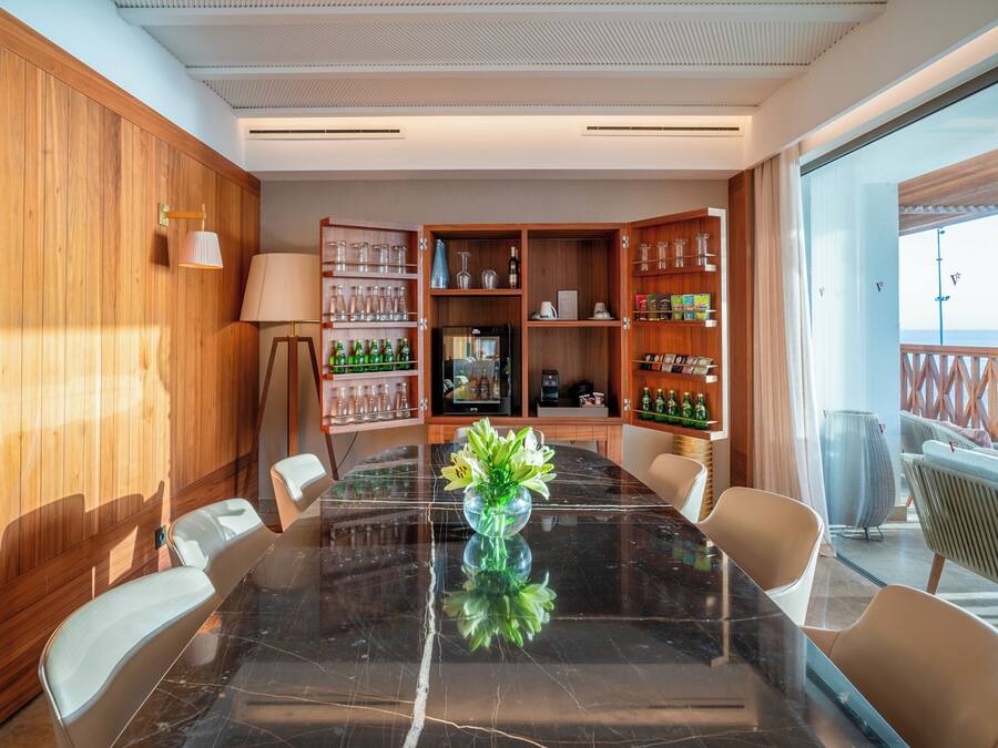 Un salón de conferencias con una mesa de mármol, sillas, una cafetera y una nevera pequeña.