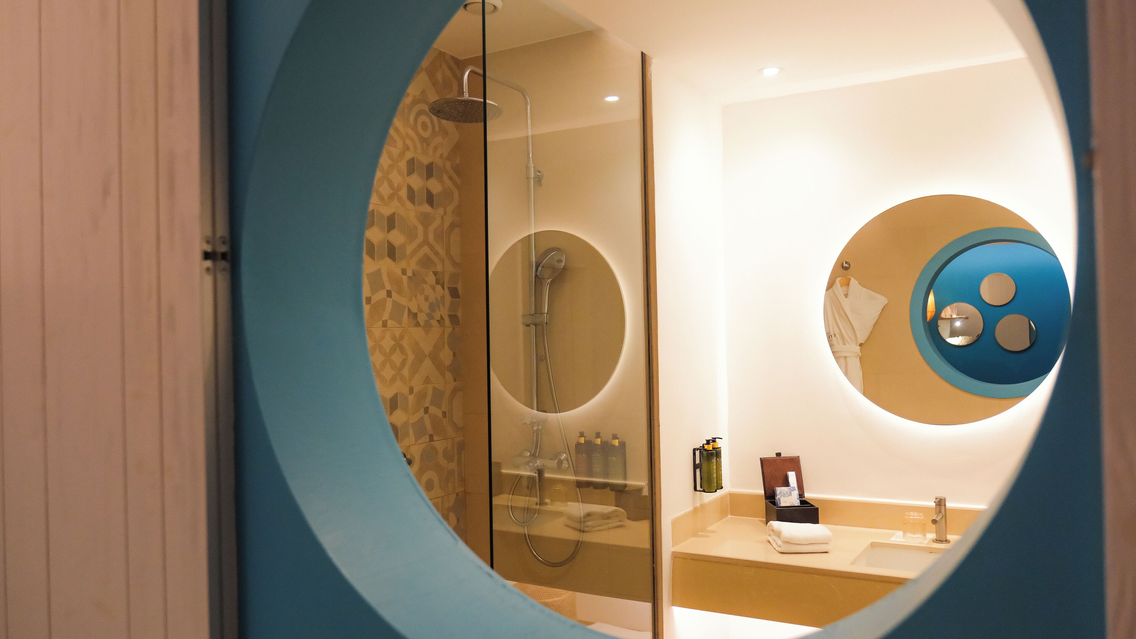 A modern bathroom with a circular mirror, a glass-enclosed shower, and a vanity with toiletries.