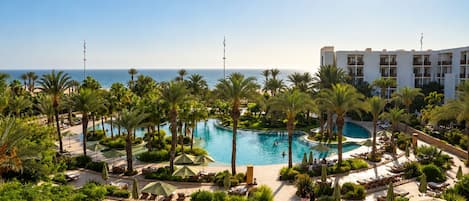 A resort with a large pool surrounded by palm trees and lounge chairs.