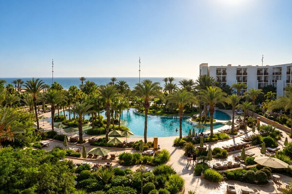 A resort with a large pool surrounded by palm trees and lounge chairs.