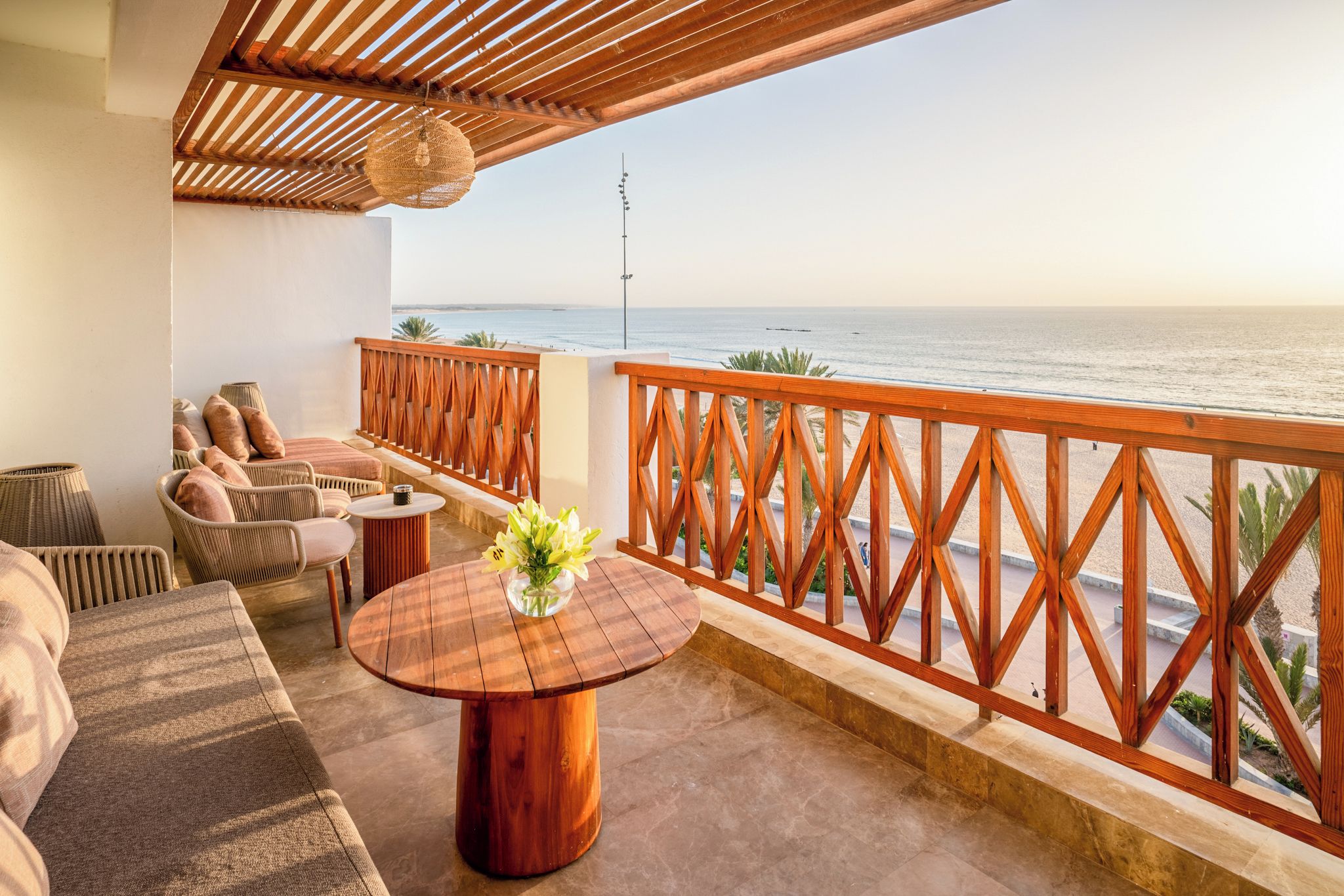A balcony with a wooden railing, wicker furniture, and a view of the sea.