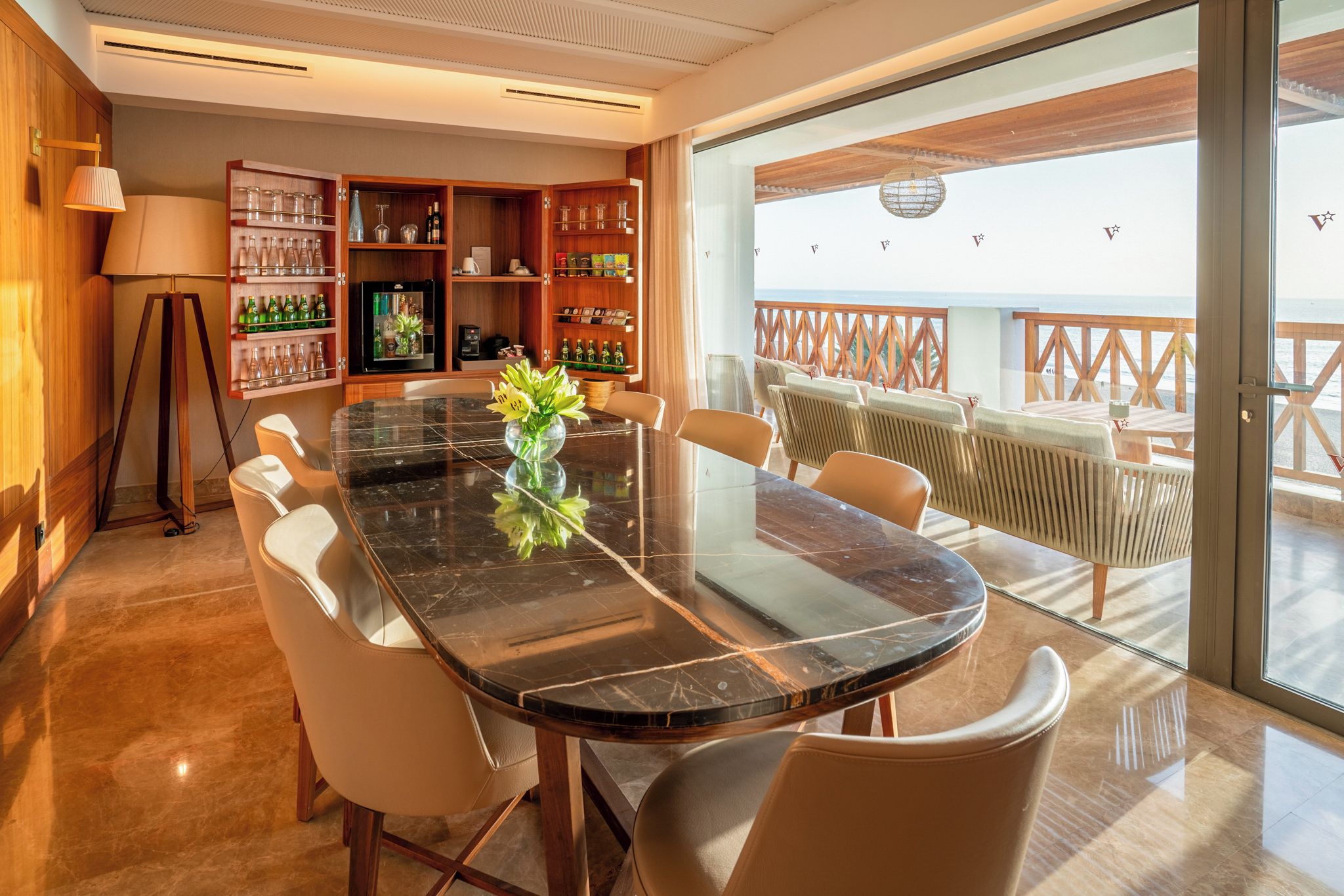 A modern dining area with a glass table, leather chairs, and a view of the sea through large windows.