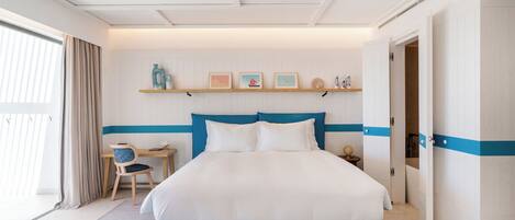 A hotel room with a large bed, a desk, and a chair. There is a shelf with decorative items above the bed.