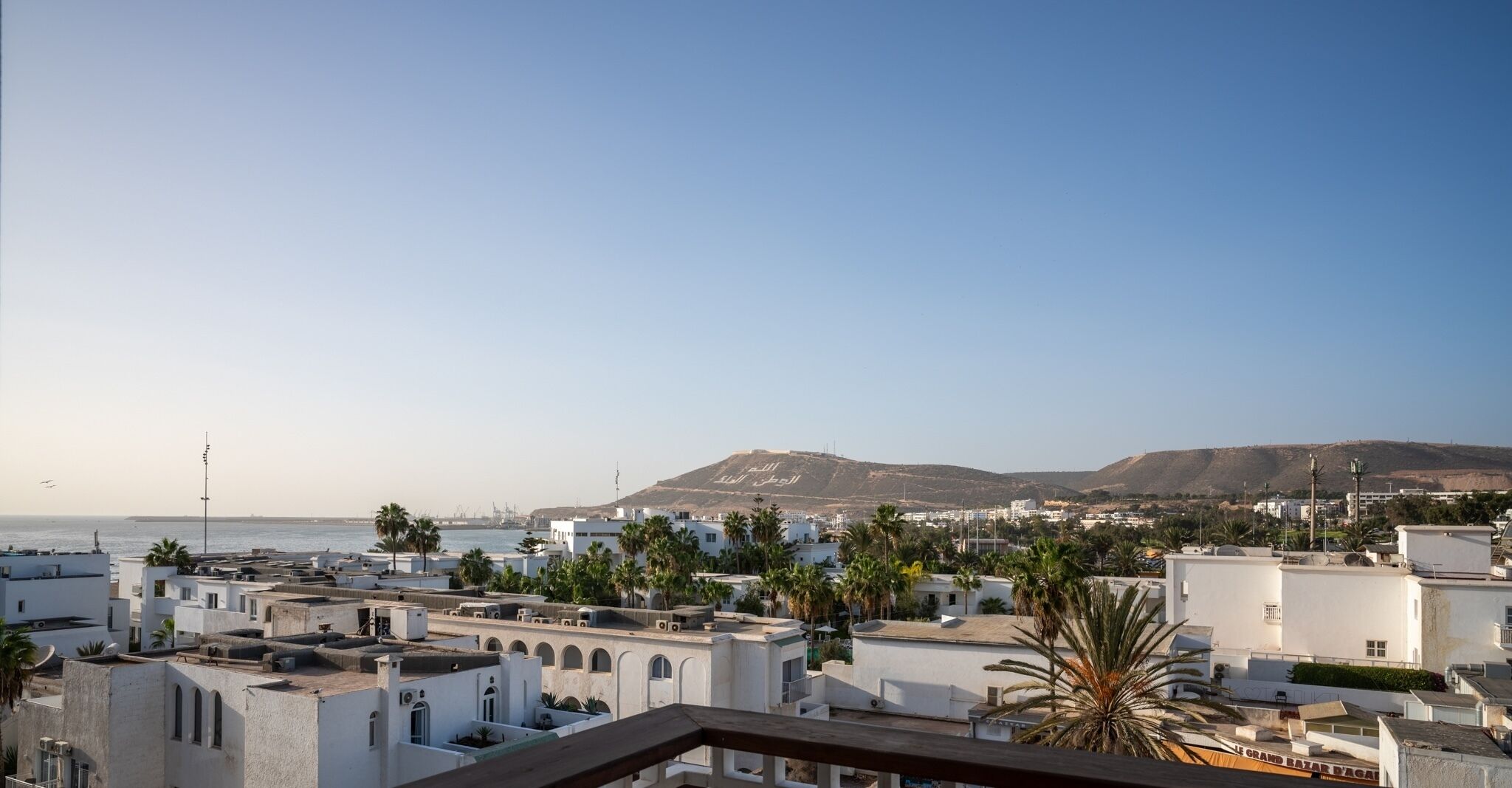 A coastal cityscape with white buildings, palm trees, and a mountain in the background.