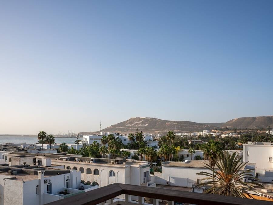 A coastal cityscape with white buildings, palm trees, and a mountain in the background.