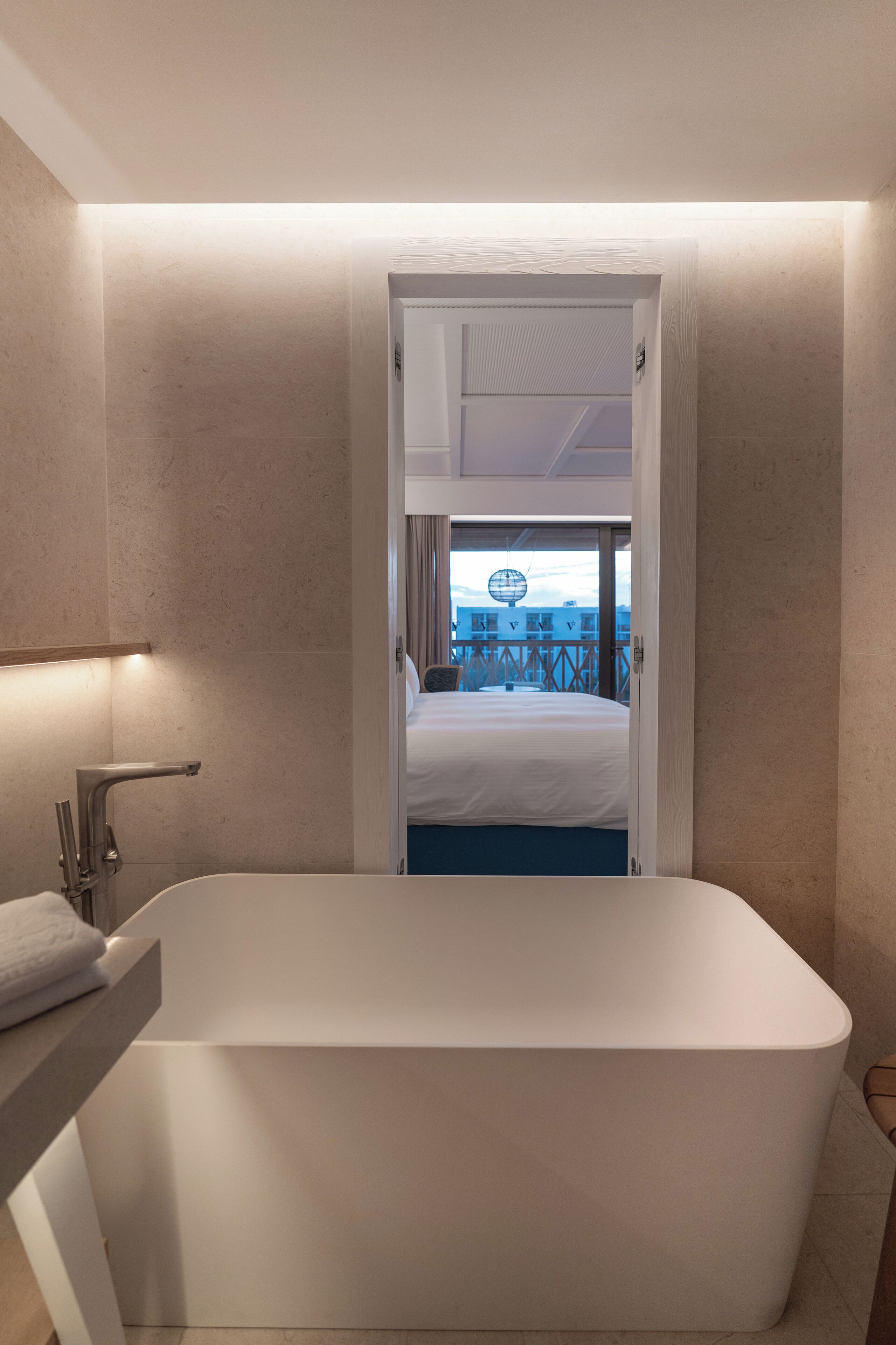 Un baño moderno con una bañera independiente, zona de ducha a la vista y vistas a un balcón con mobiliario exterior.