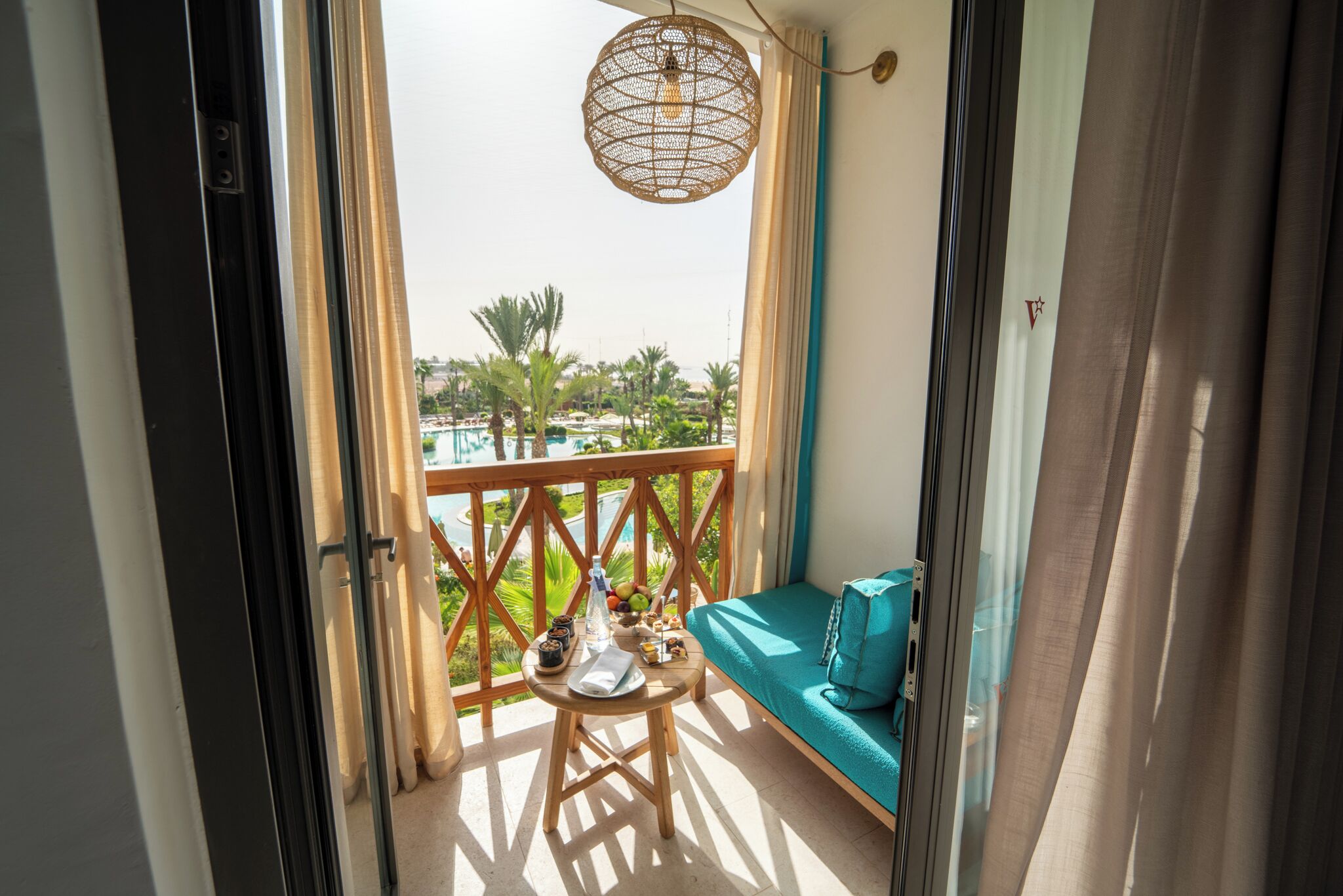 A balcony with a view of a pool, a table with a bottle, and a teal sofa.