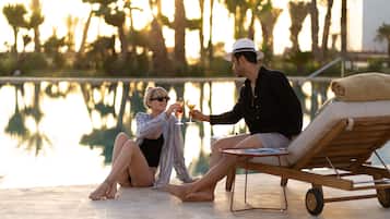 A couple relaxing by a poolside lounge chair with a towel, a table, and a glass of drink.