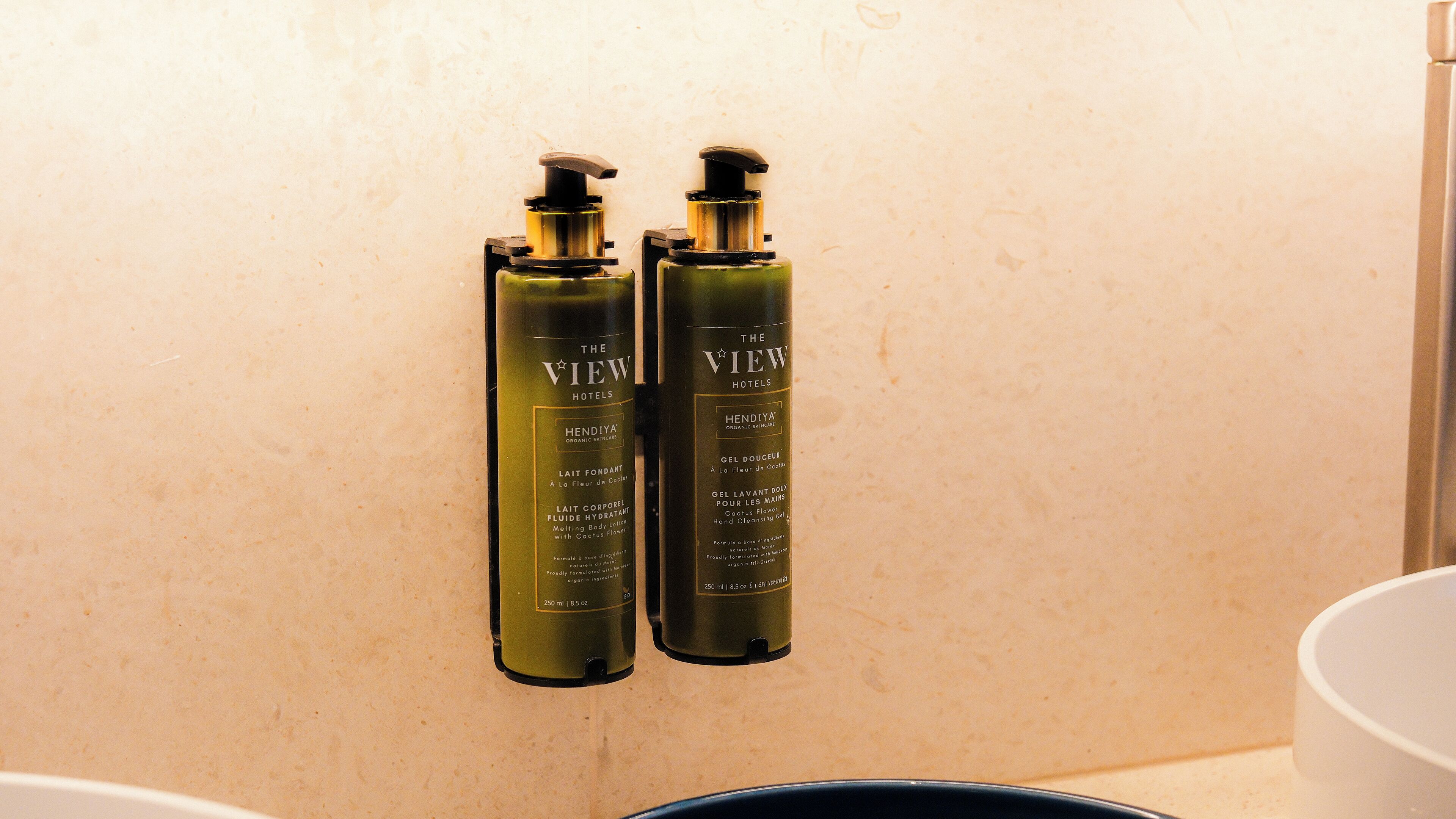 Two bottles of The View Hotels' Hendiya Organic Skincare products, including a cleansing gel and a moisturizing cream, mounted on a wall.
