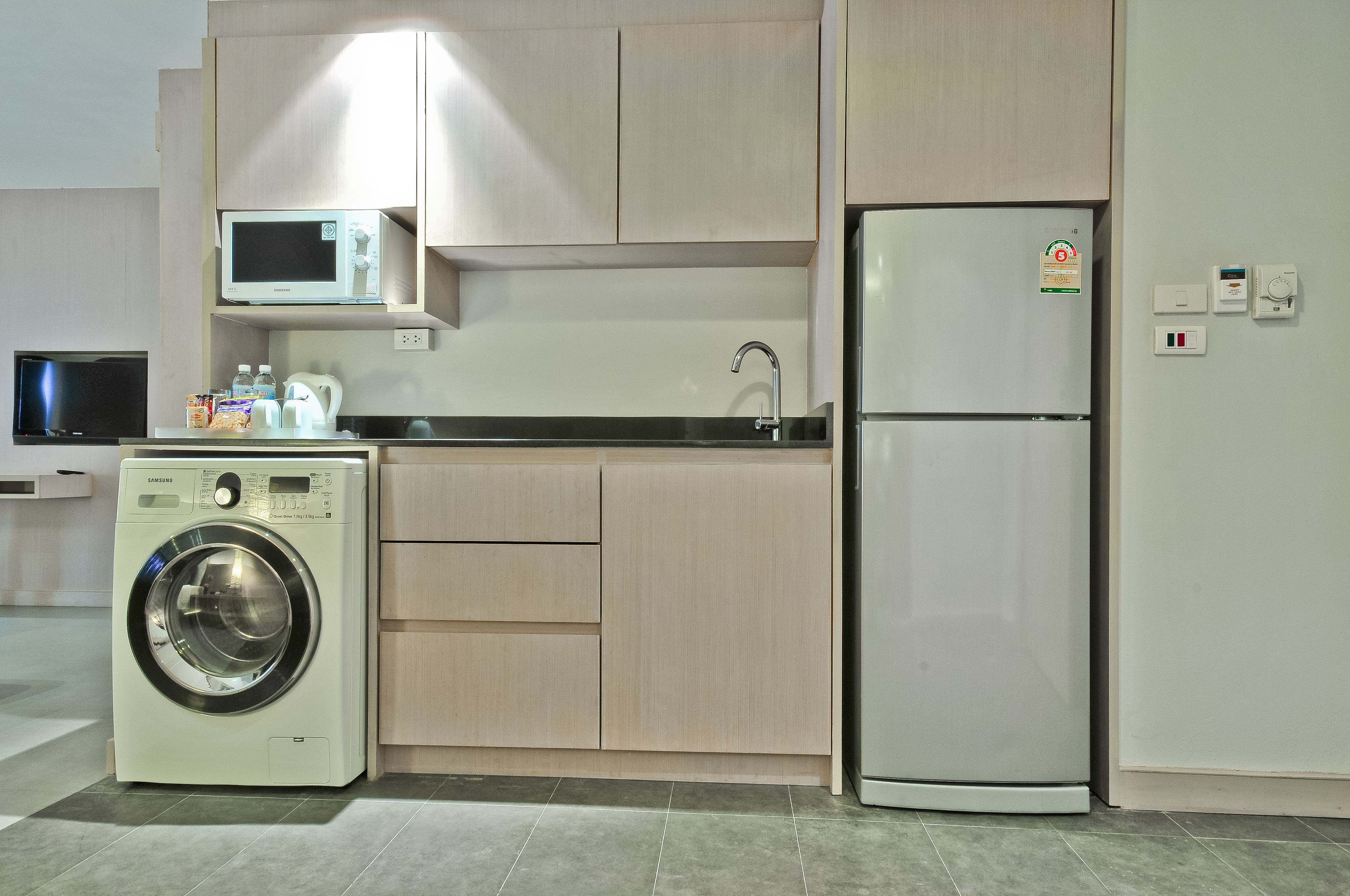 A compact kitchen with a washing machine, microwave, and refrigerator.