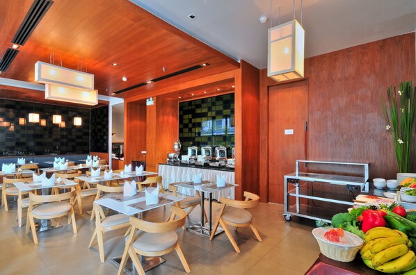 A restaurant with wooden tables and chairs, a buffet area, and a variety of fresh fruits and vegetables on display.