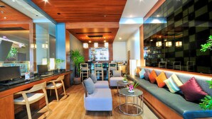 A modern bar area with a wooden ceiling, seating with colorful cushions, and a bar counter with a computer and a plant. - ASHLEE Heights Hotel Patong (Patong)