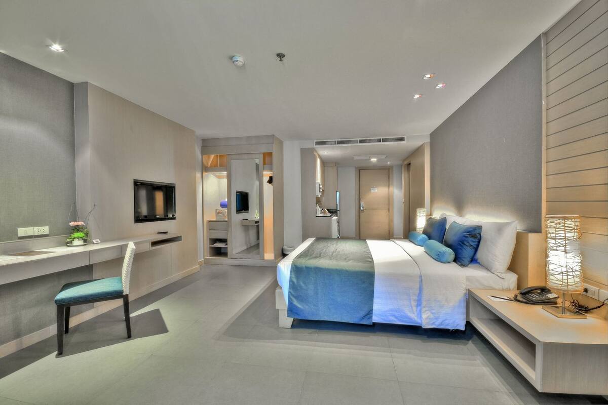 A modern hotel room with a bed, desk, chair, TV, and a walk-in closet.