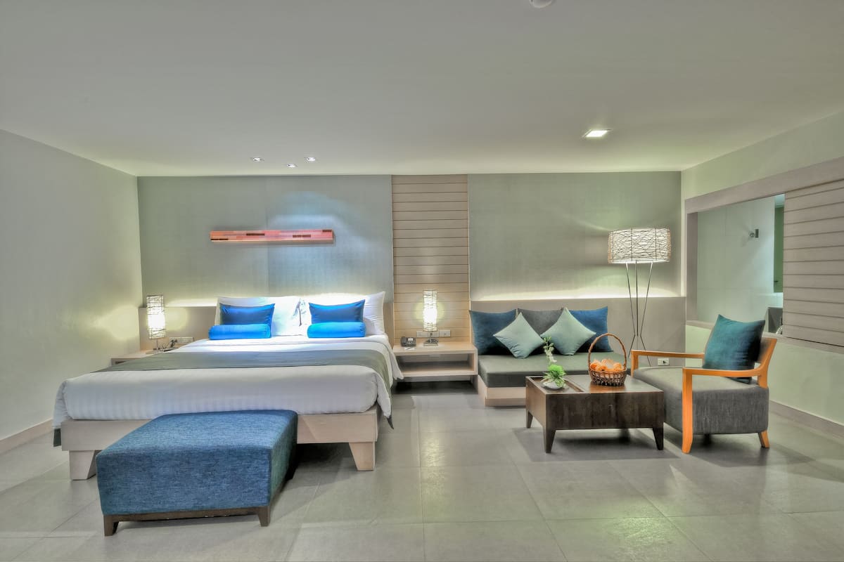 A modern hotel room with a large bed, a sofa, a small table, and a lamp.