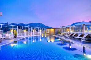 A swimming pool with lounge chairs and umbrellas, surrounded by a glass enclosure, with a view of hills in the background. - ASHLEE Heights Hotel Patong (Patong)