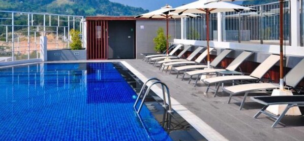 A swimming pool with lounge chairs and umbrellas, surrounded by a glass railing and a view of the hills. - ASHLEE Heights Hotel Patong (Patong)
