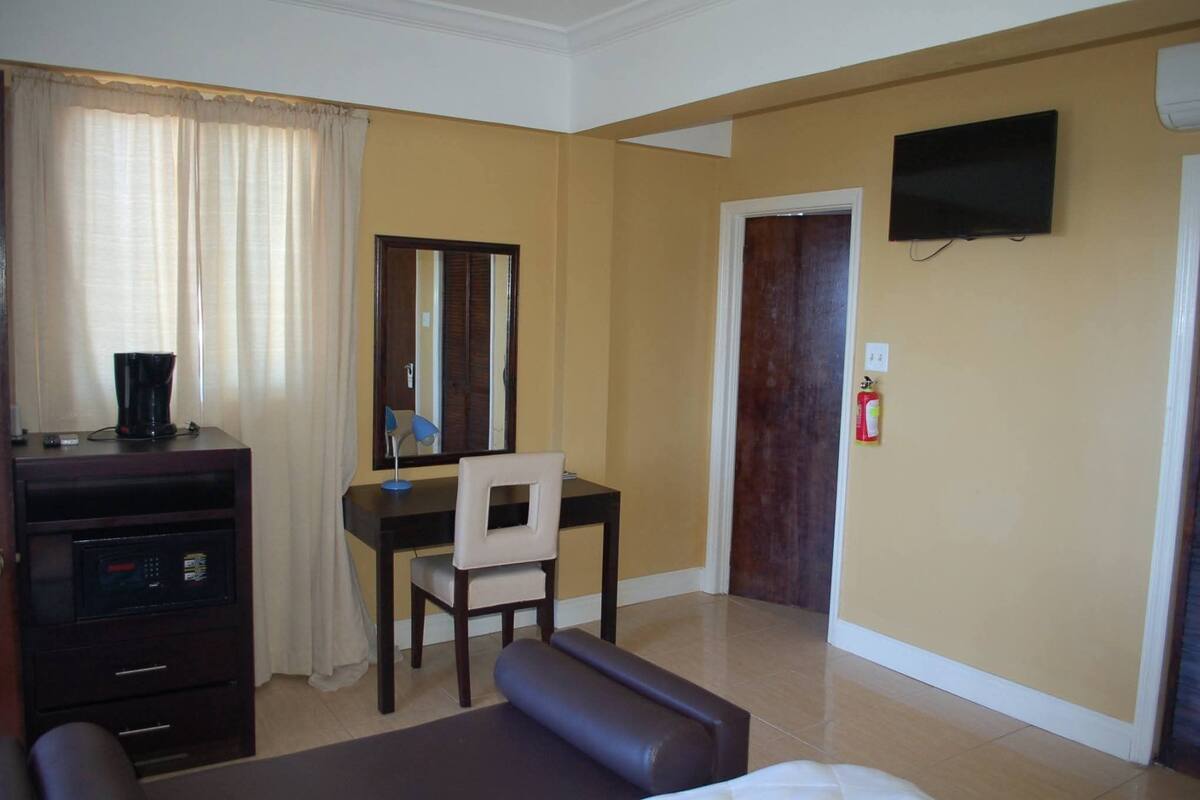 Habitación de hotel con cama, escritorio, silla, televisor y extintor.