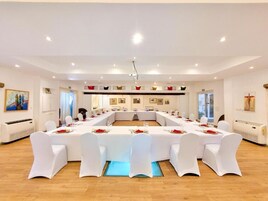 A conference room with a long table, white chairs, and red table settings.