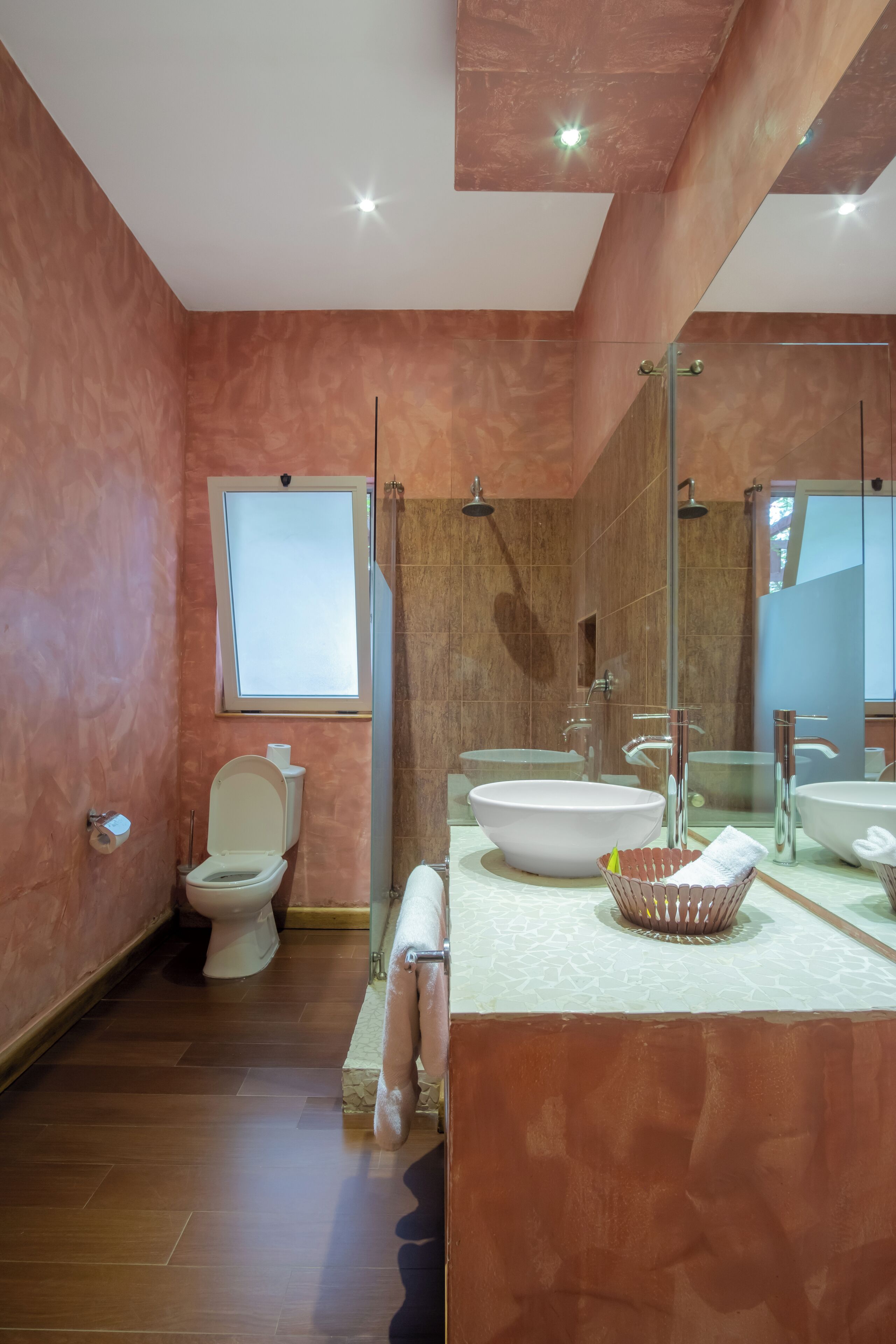 A modern bathroom with a large mirror, two sinks, a toilet, and a shower.