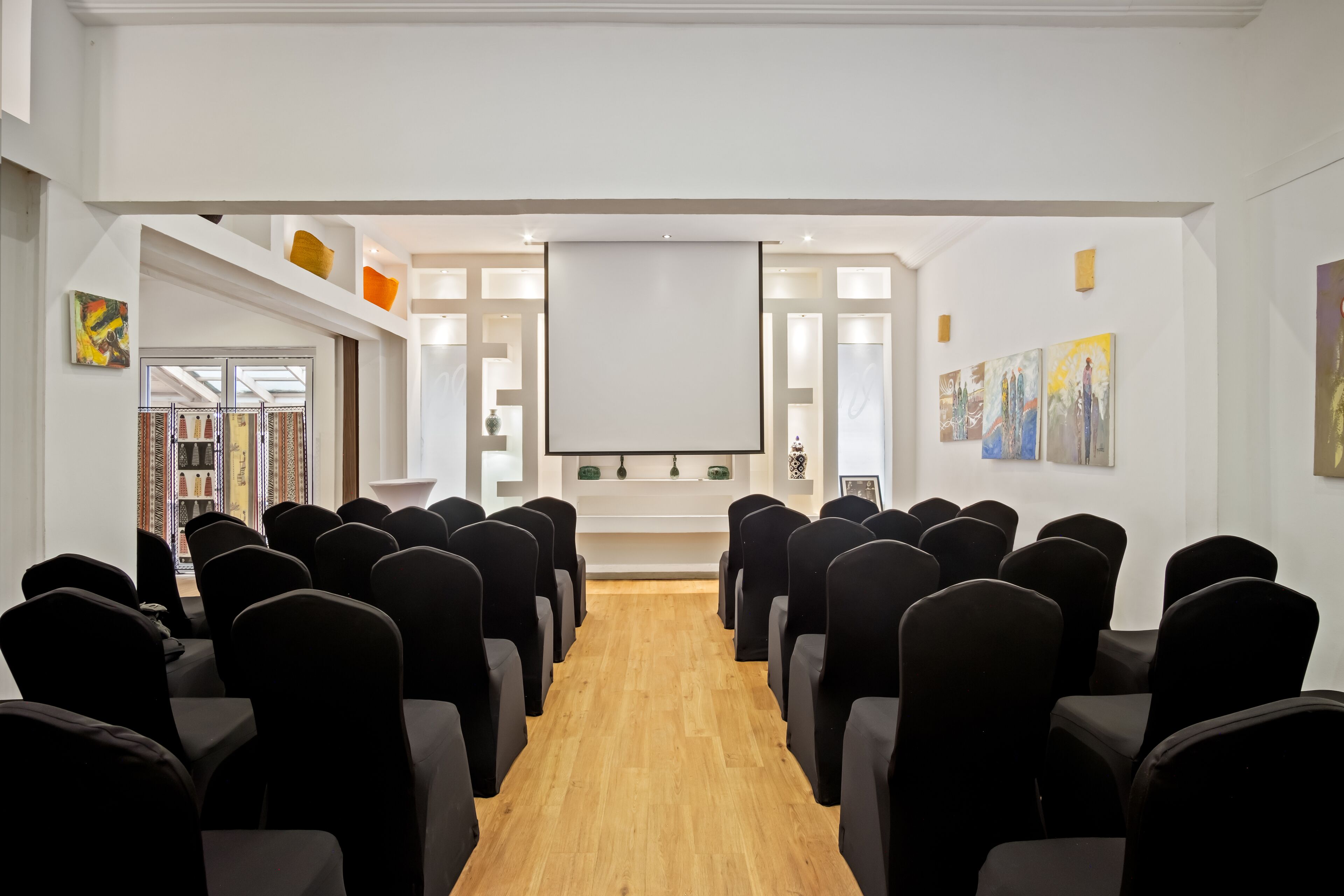 Ein Konferenzraum mit Reihen von Stühlen, die auf eine weiße Leinwand zeigen, Holzböden und Kunstwerken an den Wänden.
