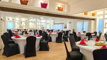 A spacious dining area with round tables, black chairs, and red napkins.