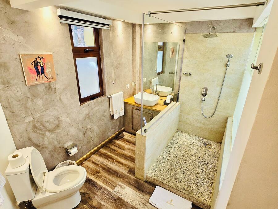 Un baño moderno con suelo de madera, un inodoro, un lavabo, una ducha con puerta de cristal y una ventana pequeña.