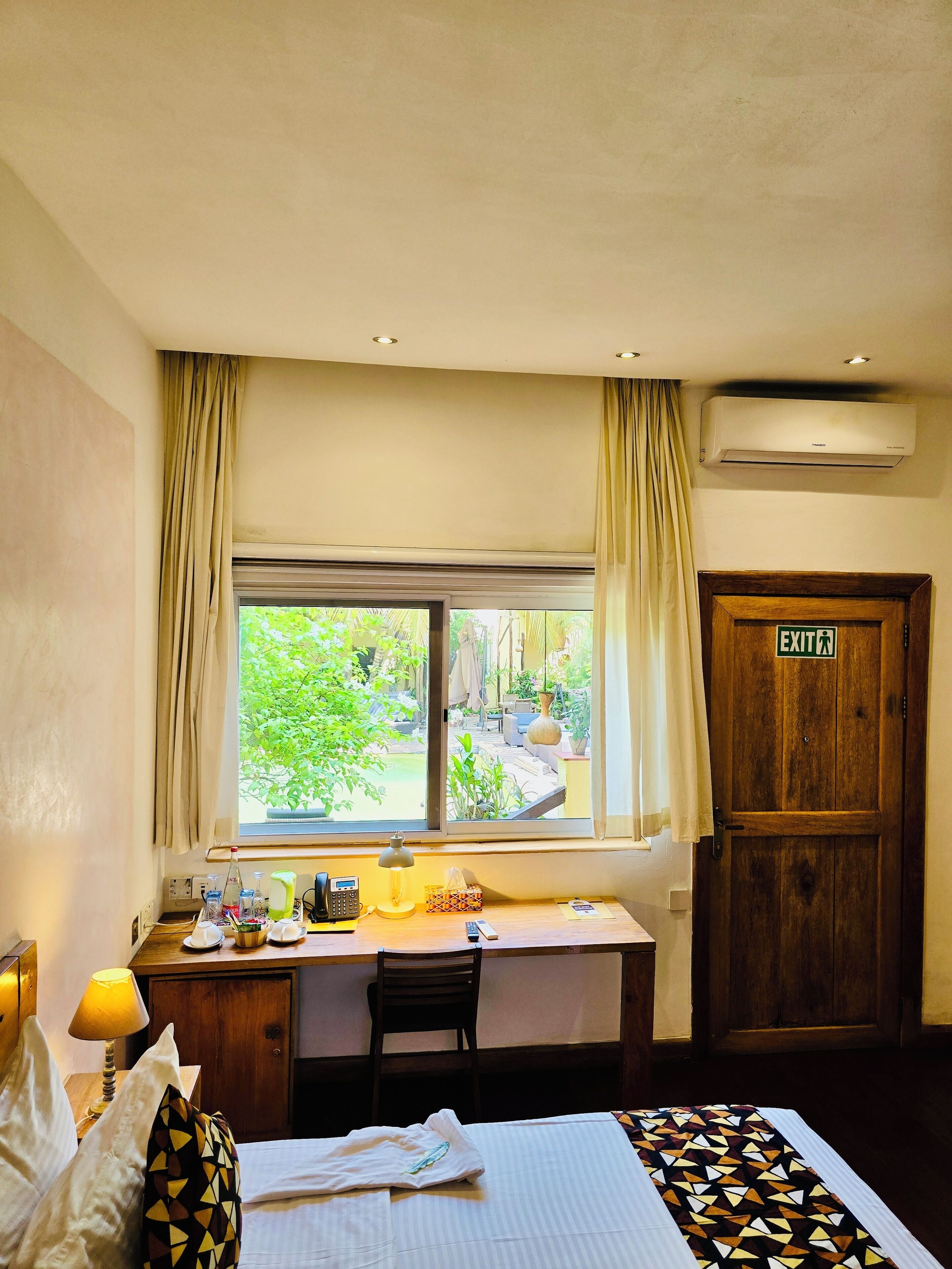 A hotel room with a bed, desk, chair, and an exit door.