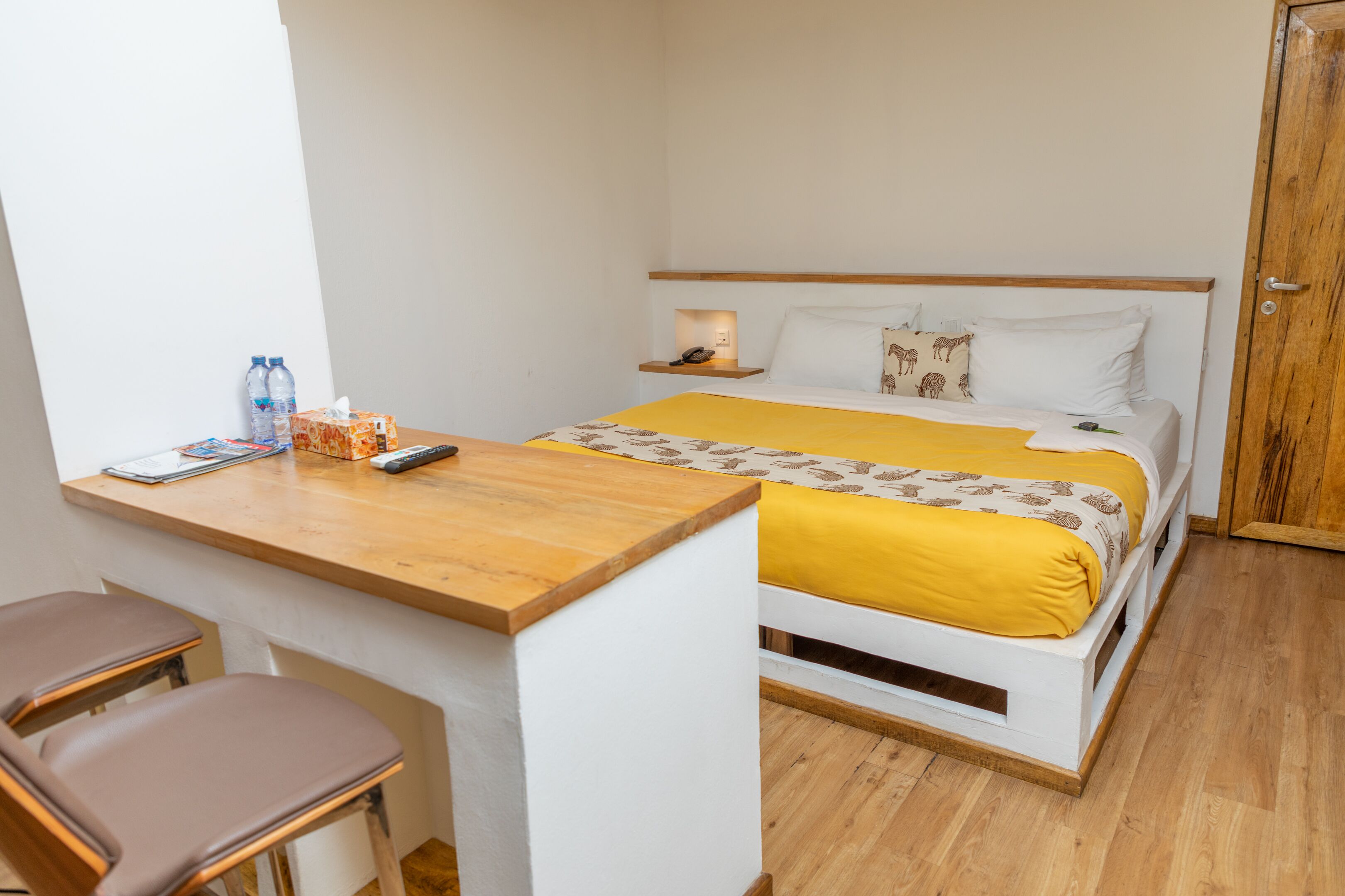 A small hotel room with a bed, a wooden desk, two chairs, and a wardrobe.