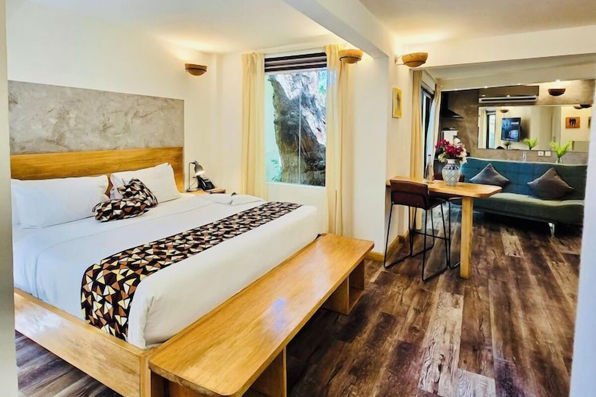 A modern hotel room with a wooden bed, a bench, a dining table, and a sofa.