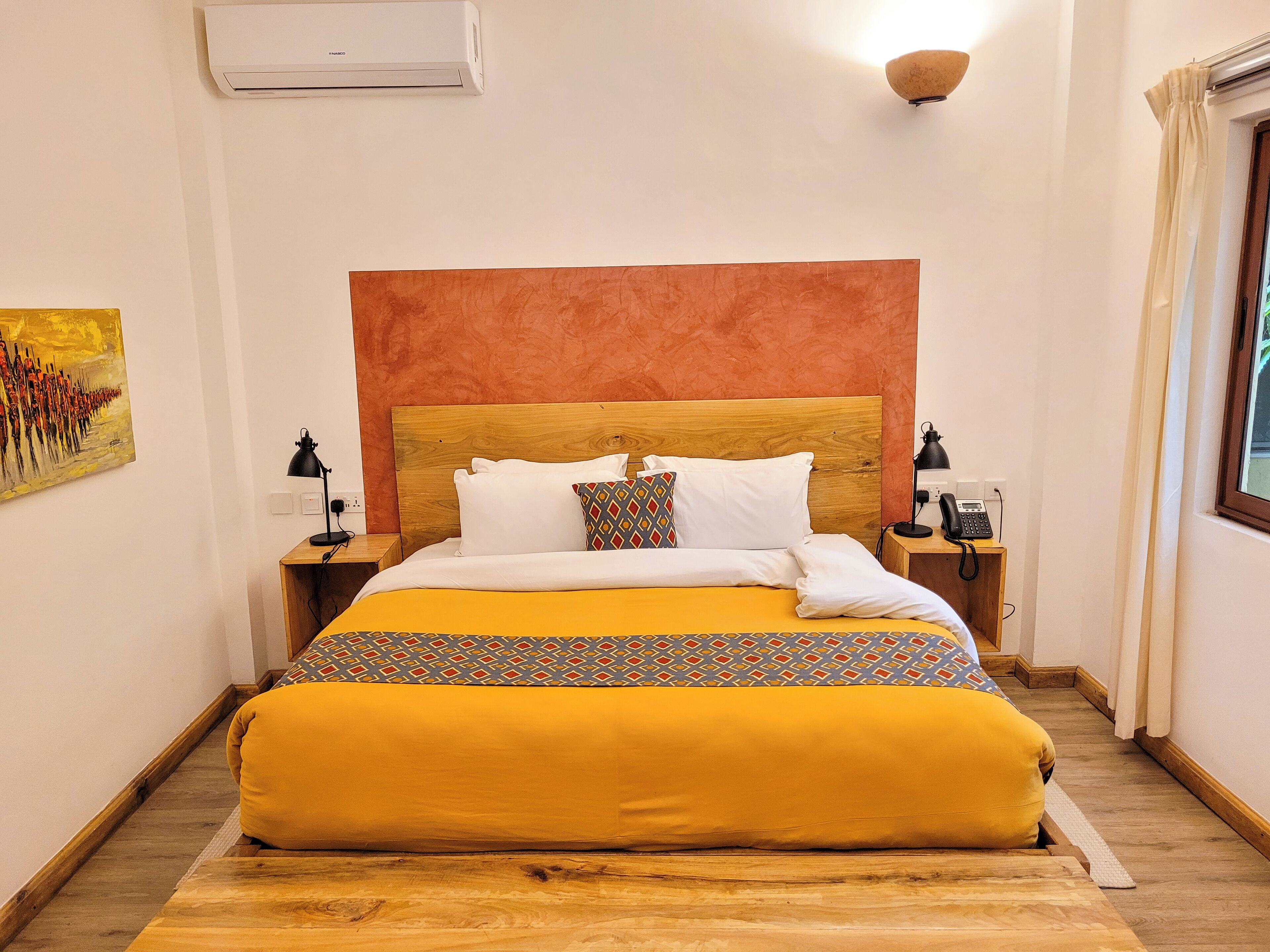 A bed with a wooden headboard, a patterned bedspread, and a bedside table with a lamp and phone.