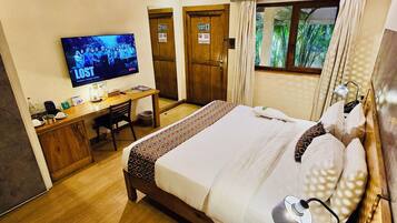 A hotel room with a bed, bedside table, lamp, desk, TV, and two doors.