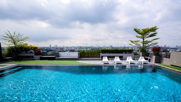 A rooftop swimming pool with clear blue water, surrounded by white lounge chairs and potted plants. - Bangkok Inter Place Hotel (Bangkok)