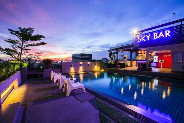 Allasalue, jossa on aurinkotuoleja ja baari nimeltä ”SKY BAR”. Taustalla näkyy kaupungin siluetti.