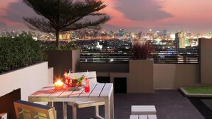 A rooftop terrace with a table set for dining, a candle, and a view of a cityscape at dusk. - Bangkok Inter Place Hotel (Bangkok)