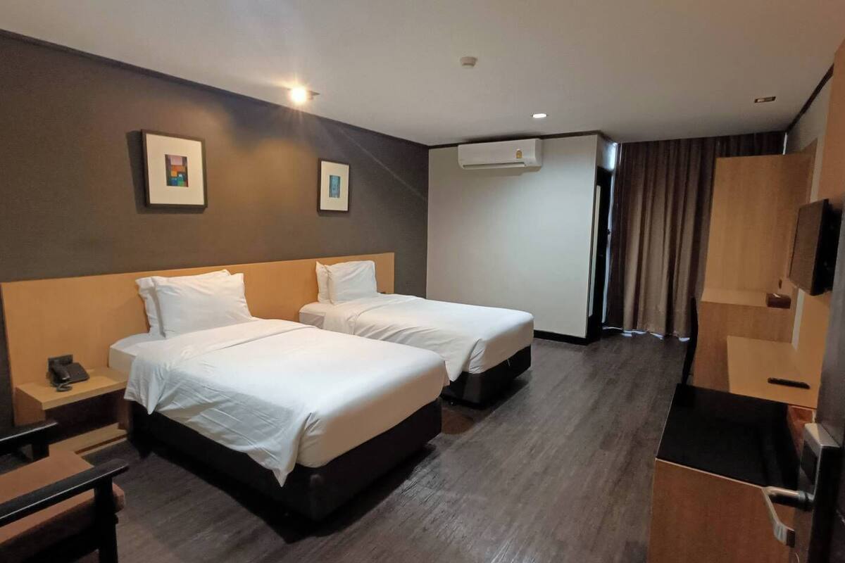Une chambre d’hôtel avec deux lits, un bureau, une chaise, un appareil de climatisation et un téléviseur.