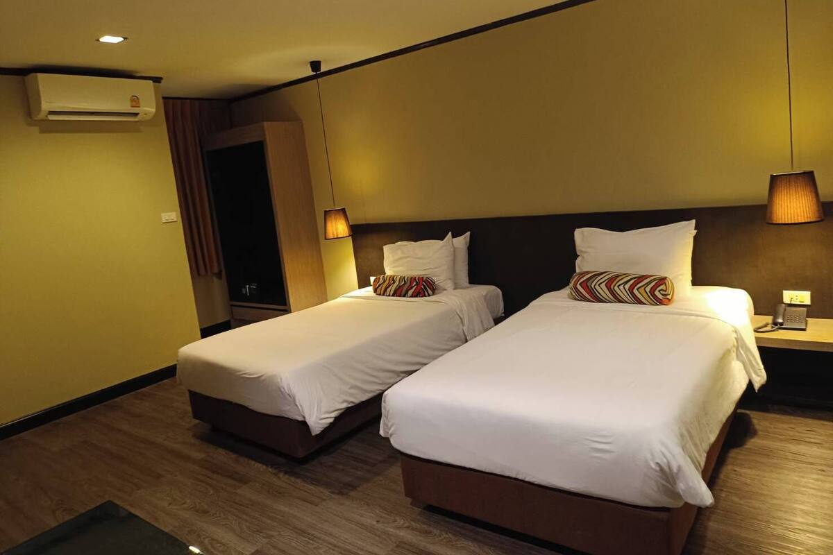 Une chambre d’hôtel avec deux lits simples, une table de chevet avec une lampe, un appareil de climatisation et un plancher en bois.