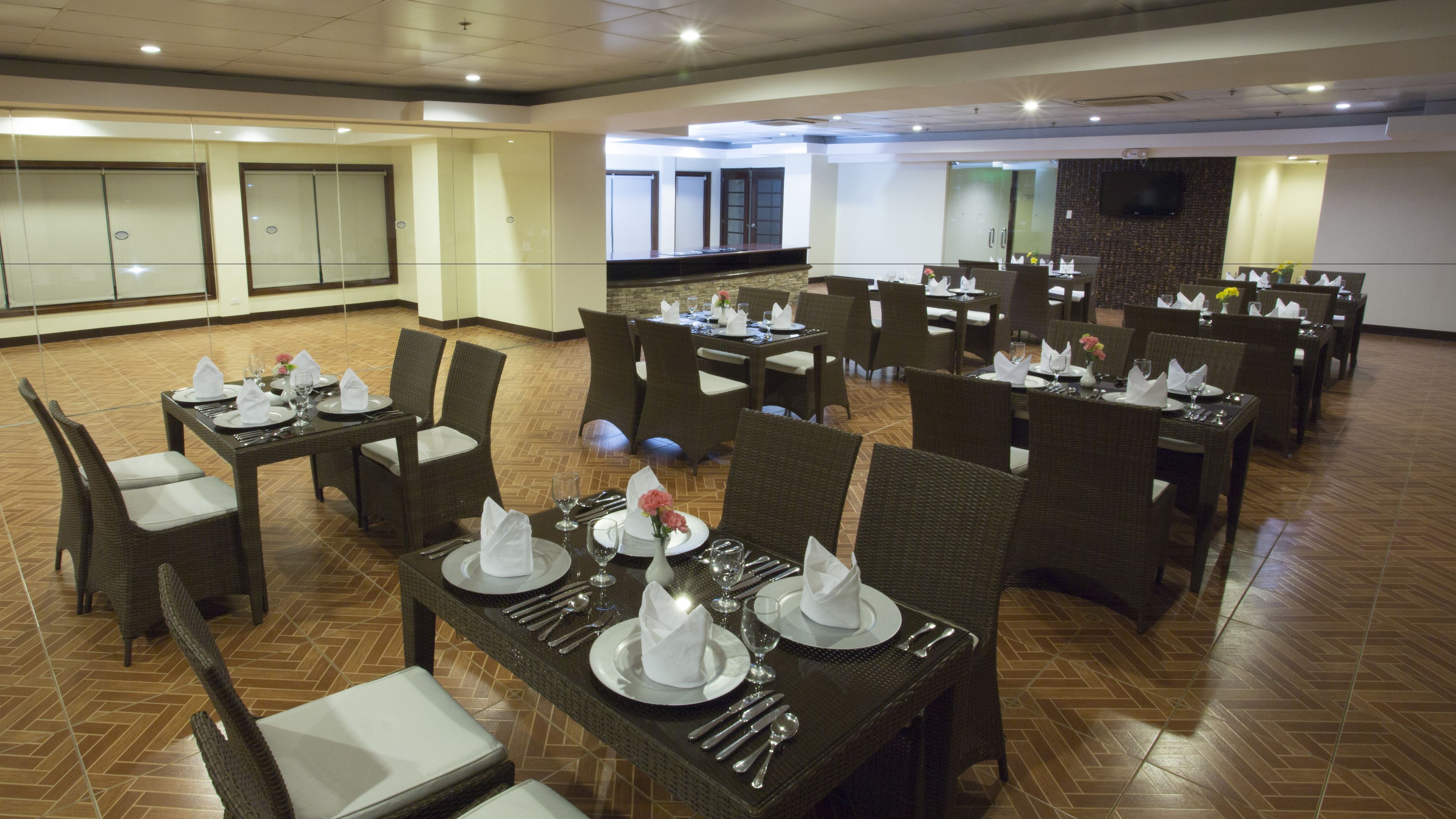 A spacious dining area with multiple tables set for dining, featuring wicker chairs and a polished herringbone floor.