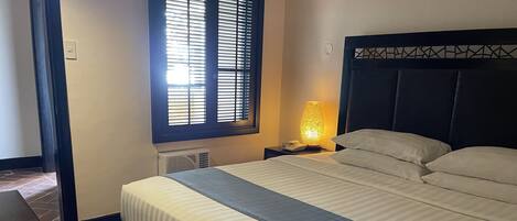A neatly made bed with a striped bedspread, a bedside lamp, and a window with blinds.