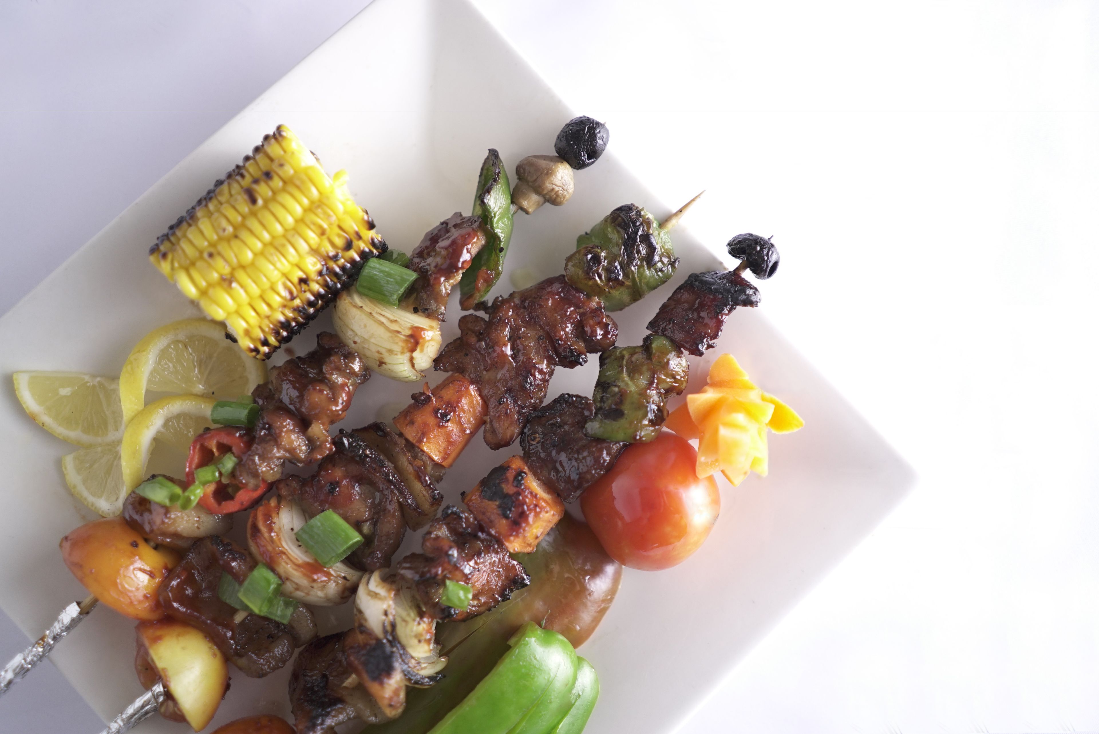 A plate of grilled skewers with vegetables and corn.