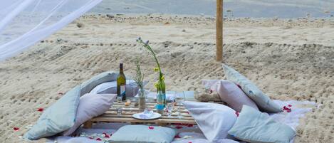 A beach picnic setup with a blanket, pillows, a bottle of wine, and a glass of water.